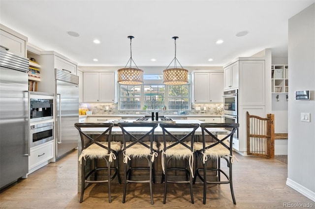 kitchen featuring a center island, hanging light fixtures, stainless steel appliances, a kitchen breakfast bar, and light wood-type flooring