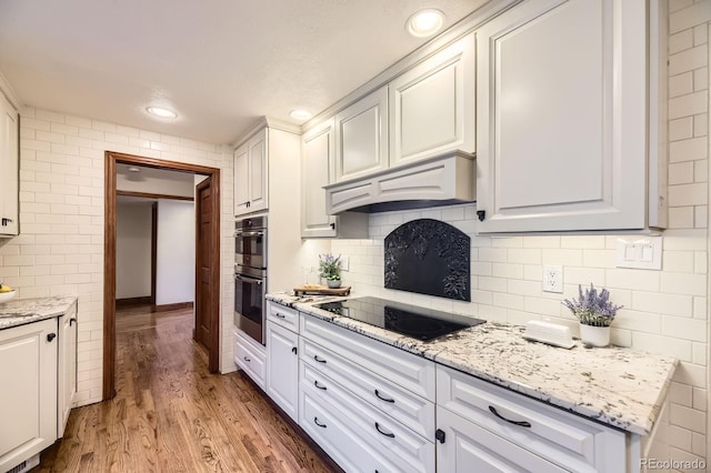5475 W Ottawa Ave, Littleton, CO 80128 - kitchen with black electric cooktop, premium range hood, double oven, light wood-type flooring, and white cabinetry