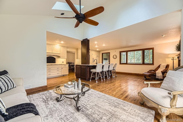 5475 W Ottawa Ave, Littleton, CO 80128 - living area featuring ceiling fan, light wood finished floors, a skylight, baseboards, and high vaulted ceiling
