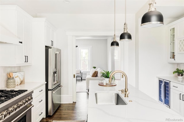 kitchen with white cabinets, premium appliances, light stone counters, and sink