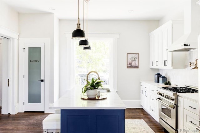 kitchen featuring dark wood-type flooring, hanging light fixtures, wall chimney range hood, high end stainless steel range, and white cabinets