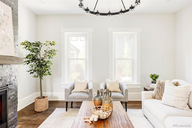 living room with dark hardwood / wood-style flooring, an inviting chandelier, and a stone fireplace