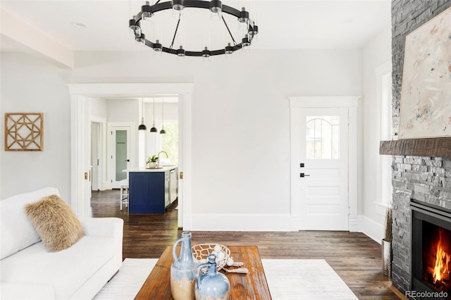 living room featuring a notable chandelier, dark hardwood / wood-style flooring, a stone fireplace, and plenty of natural light