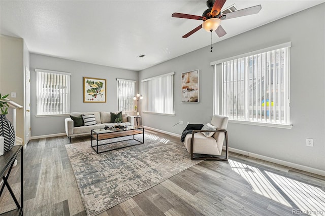 living area featuring baseboards, a ceiling fan, visible vents, and wood finished floors