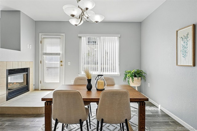 dining space with a fireplace, an inviting chandelier, baseboards, and wood finished floors