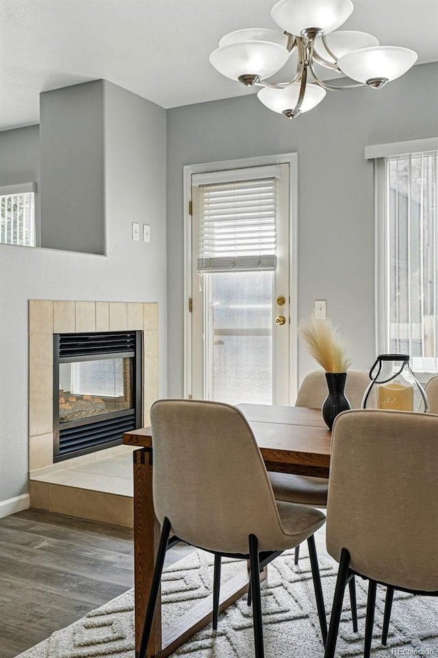 dining area with baseboards, a tile fireplace, a chandelier, and wood finished floors