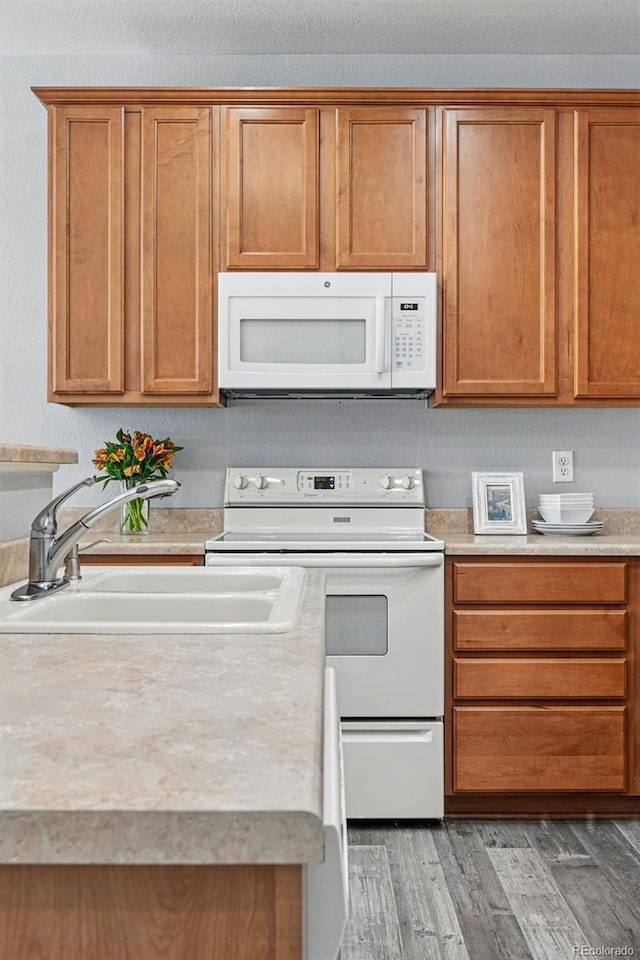 kitchen with a sink, brown cabinetry, white appliances, light wood finished floors, and light countertops