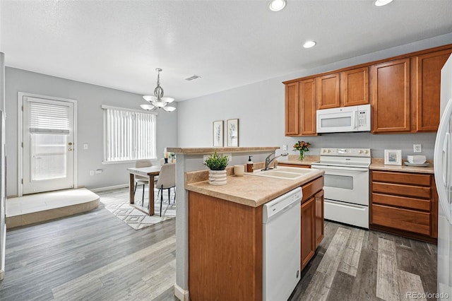 kitchen with an inviting chandelier, brown cabinets, light wood-style flooring, a sink, and white appliances