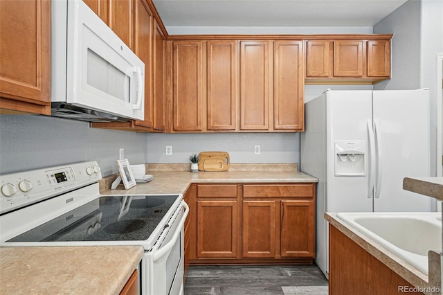kitchen with wood finished floors, a sink, brown cabinetry, white appliances, and light countertops