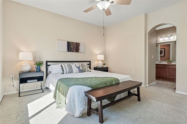 bedroom with baseboards, ceiling fan, arched walkways, ensuite bath, and light carpet