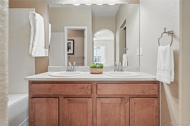 full bathroom featuring a tub to relax in, double vanity, a sink, and a textured wall