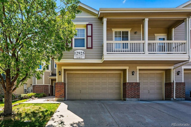 view of property featuring an attached garage, brick siding, driveway, and a balcony