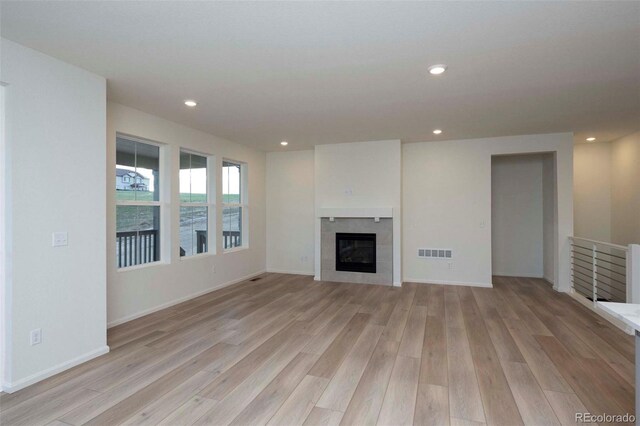 unfurnished living room with light wood-type flooring and a tiled fireplace