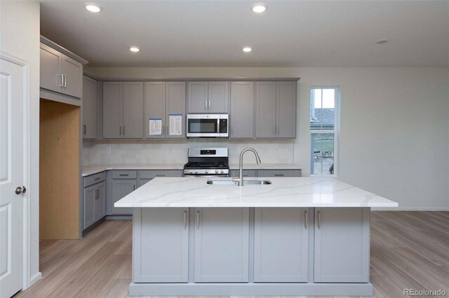 kitchen with gray cabinets, light wood-type flooring, sink, stainless steel appliances, and light stone countertops