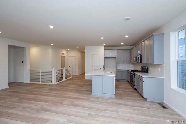 kitchen featuring gray cabinets, a kitchen island with sink, tasteful backsplash, light hardwood / wood-style flooring, and stainless steel appliances