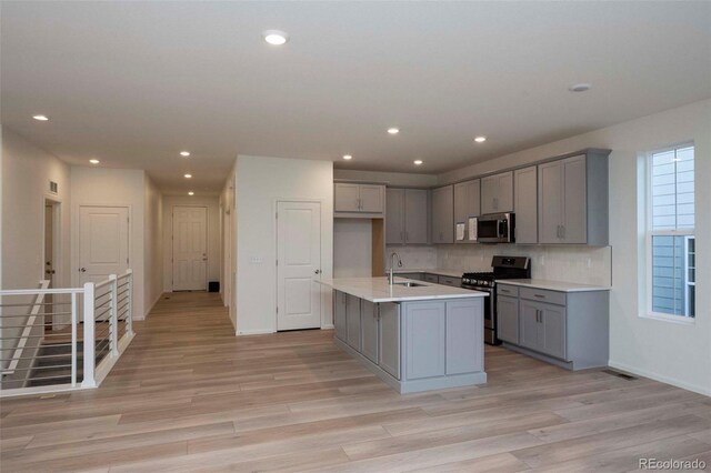 kitchen featuring appliances with stainless steel finishes, gray cabinetry, light hardwood / wood-style floors, a kitchen island with sink, and sink