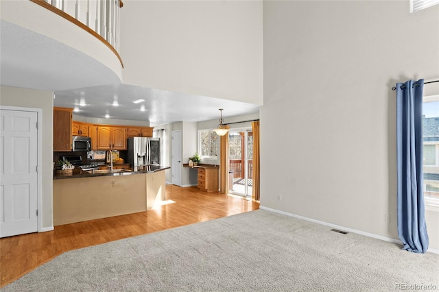 kitchen with hanging light fixtures, kitchen peninsula, light colored carpet, decorative backsplash, and appliances with stainless steel finishes