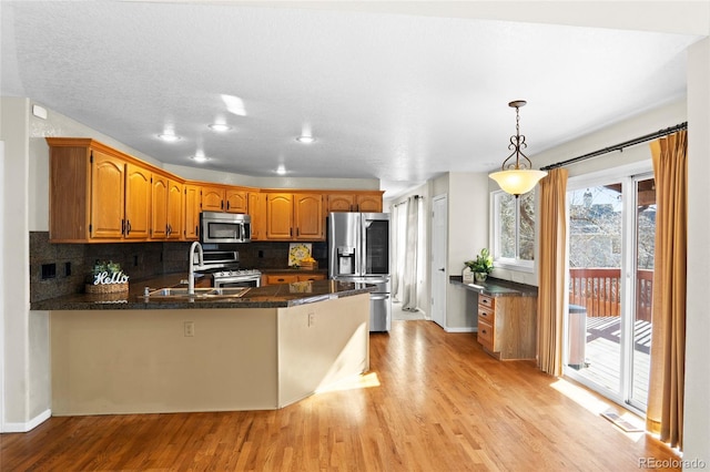 kitchen with kitchen peninsula, appliances with stainless steel finishes, light wood-type flooring, sink, and pendant lighting