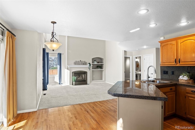 kitchen with kitchen peninsula, tasteful backsplash, sink, light hardwood / wood-style floors, and hanging light fixtures