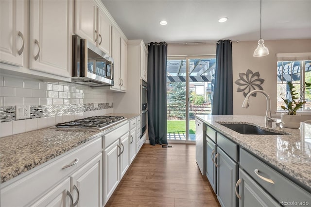 kitchen with appliances with stainless steel finishes, a sink, white cabinets, gray cabinets, and tasteful backsplash