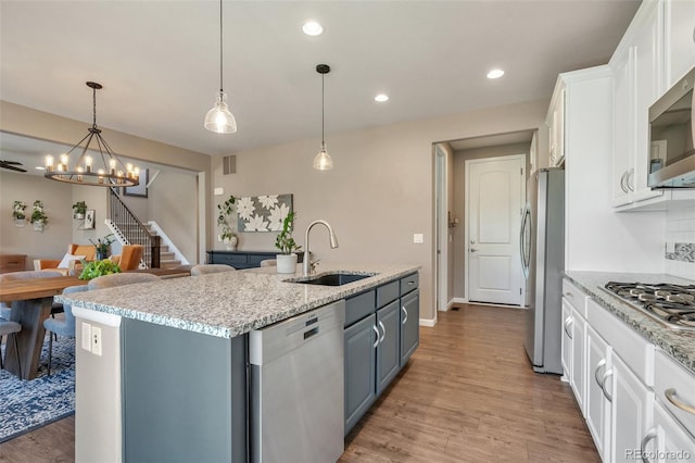 kitchen featuring stainless steel appliances, a sink, a chandelier, white cabinetry, and light wood finished floors