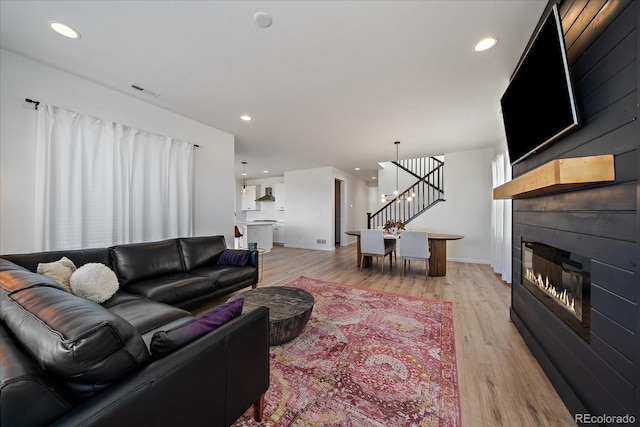 living area with visible vents, a large fireplace, stairs, recessed lighting, and light wood-style flooring