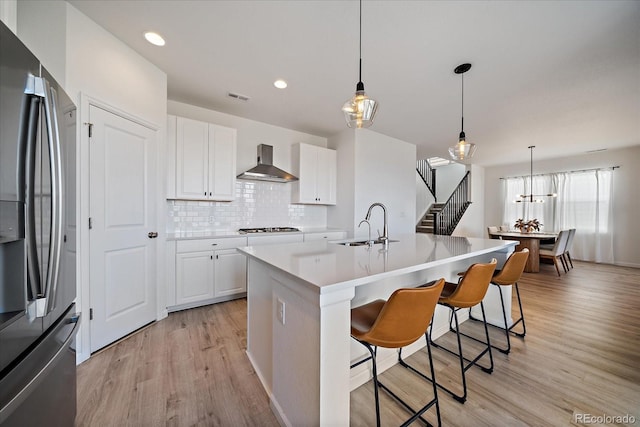 kitchen with visible vents, stainless steel refrigerator with ice dispenser, light wood-type flooring, wall chimney exhaust hood, and a sink
