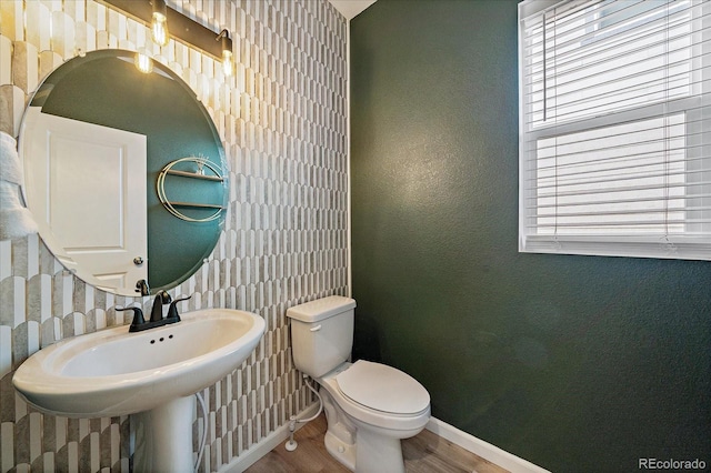 half bathroom with a healthy amount of sunlight, baseboards, toilet, and wood finished floors