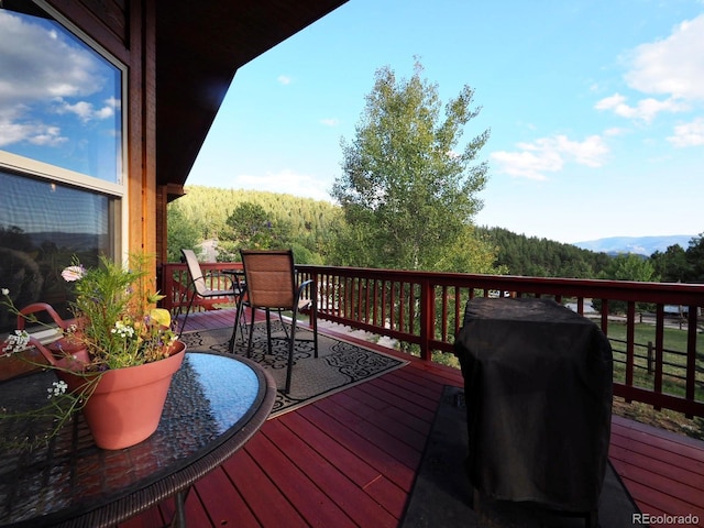 deck featuring outdoor dining area, a view of trees, and area for grilling