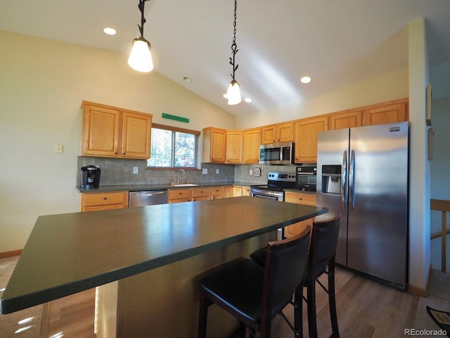 kitchen featuring a breakfast bar area, stainless steel appliances, dark countertops, tasteful backsplash, and a sink