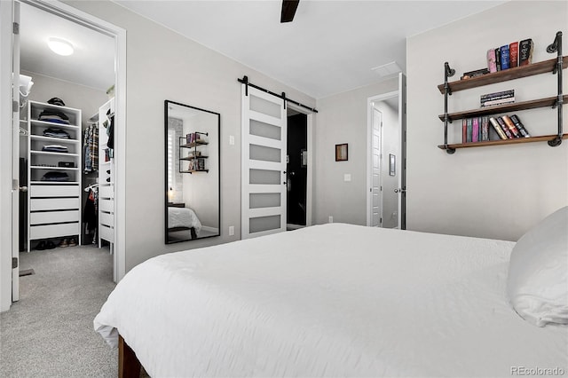bedroom featuring a closet, ceiling fan, a barn door, a spacious closet, and carpet flooring