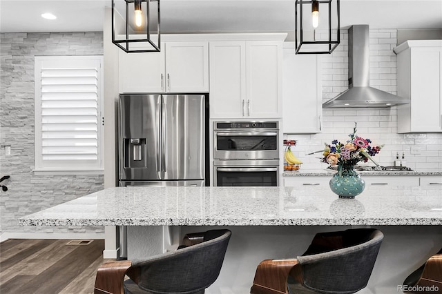 kitchen featuring appliances with stainless steel finishes, wood finished floors, white cabinets, a breakfast bar, and wall chimney exhaust hood