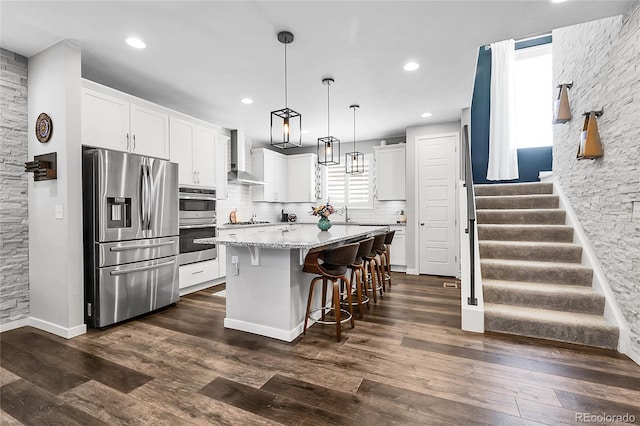 kitchen featuring wall chimney range hood, white cabinets, a center island, stainless steel appliances, and decorative backsplash