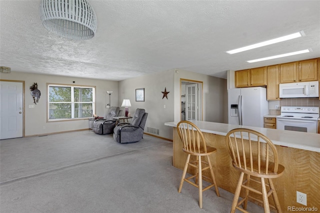 kitchen featuring white appliances, baseboards, a textured ceiling, open floor plan, and a kitchen breakfast bar