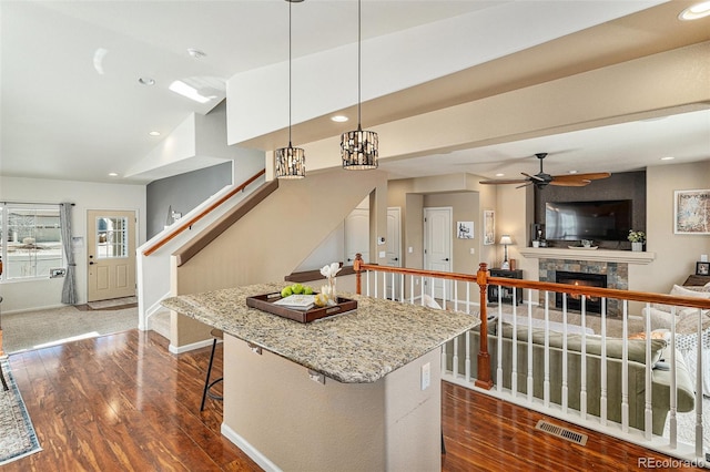 kitchen with a breakfast bar area, recessed lighting, a fireplace, visible vents, and dark wood finished floors