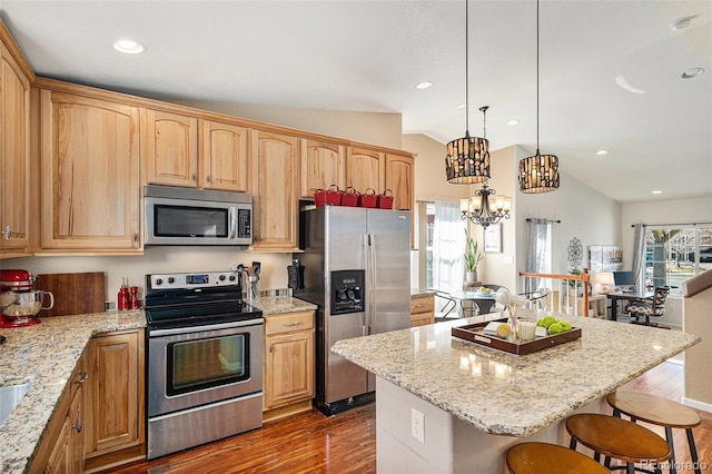 kitchen with a kitchen breakfast bar, vaulted ceiling, appliances with stainless steel finishes, light stone countertops, and dark wood-style floors