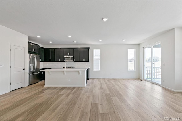 kitchen featuring stainless steel appliances, light hardwood / wood-style flooring, decorative backsplash, a breakfast bar, and a center island with sink