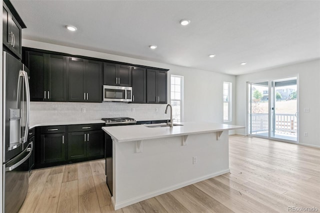 kitchen featuring appliances with stainless steel finishes, light wood-type flooring, tasteful backsplash, sink, and an island with sink