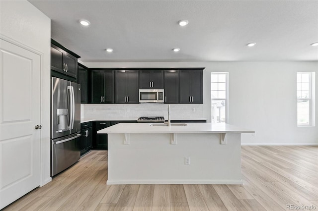 kitchen featuring sink, stainless steel appliances, a kitchen island with sink, and light hardwood / wood-style flooring