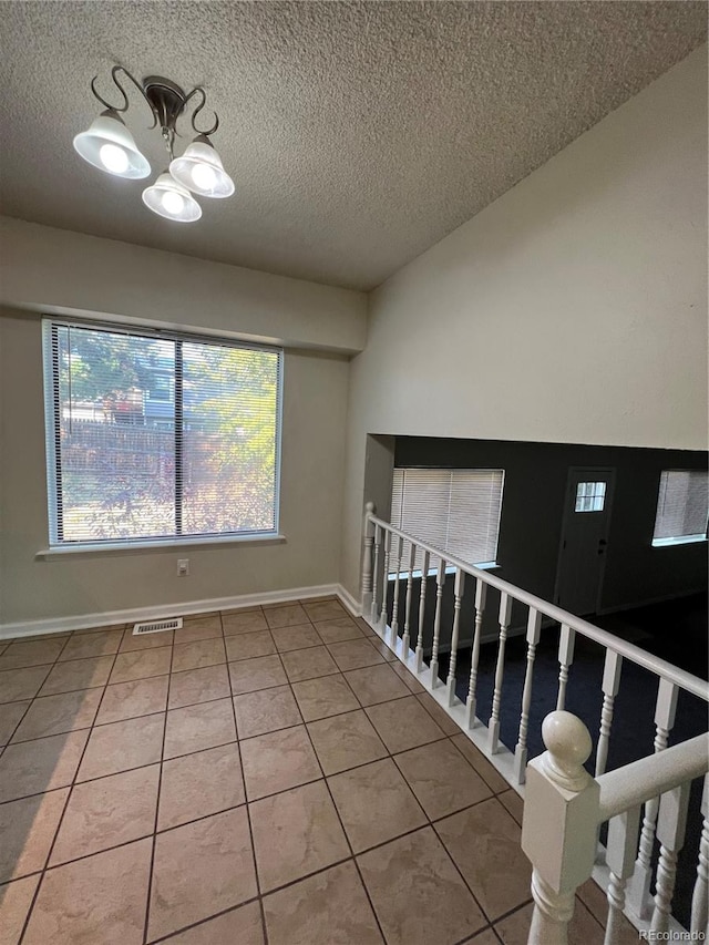 tiled empty room with a notable chandelier and a textured ceiling