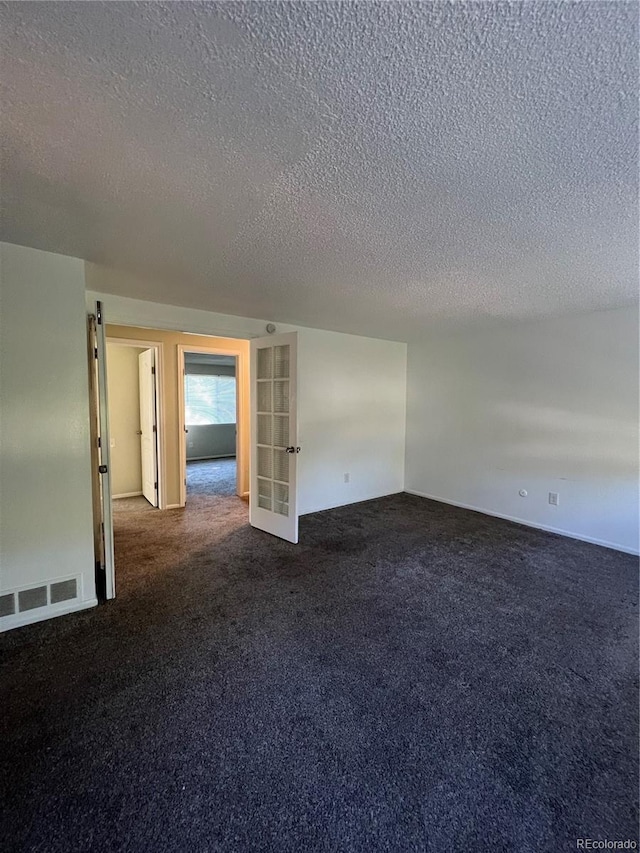 spare room with a textured ceiling and dark colored carpet