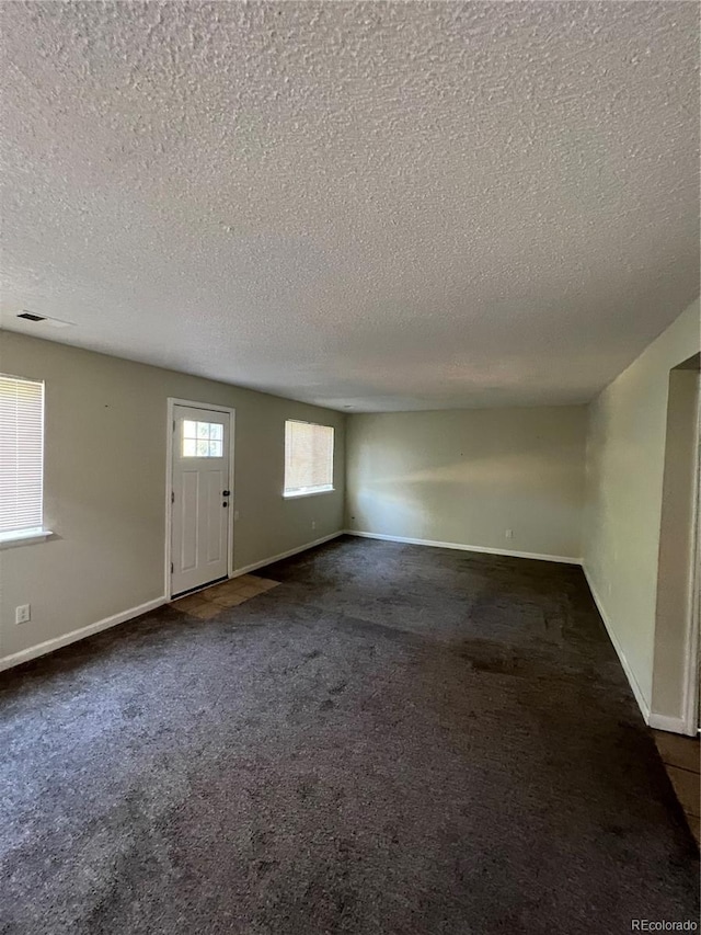 interior space featuring a textured ceiling and dark colored carpet