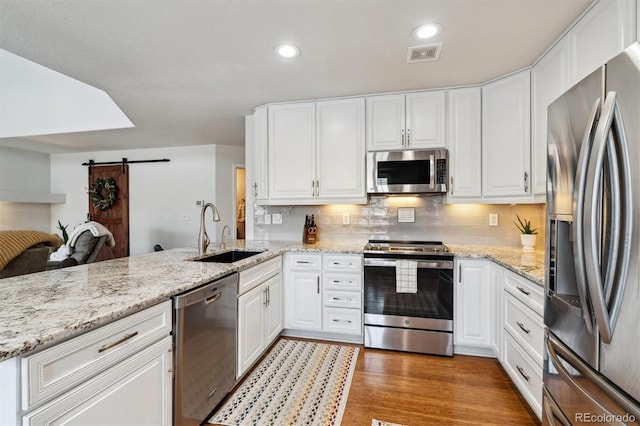 kitchen with white cabinetry, appliances with stainless steel finishes, a barn door, and sink