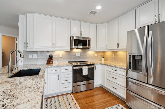 kitchen featuring stainless steel appliances, white cabinetry, sink, and light stone counters