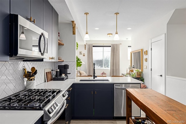 kitchen featuring a sink, decorative light fixtures, tasteful backsplash, appliances with stainless steel finishes, and a peninsula