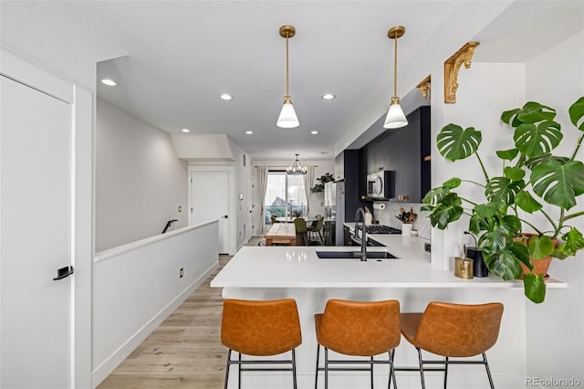 kitchen featuring a sink, dark cabinetry, stainless steel appliances, a peninsula, and light countertops