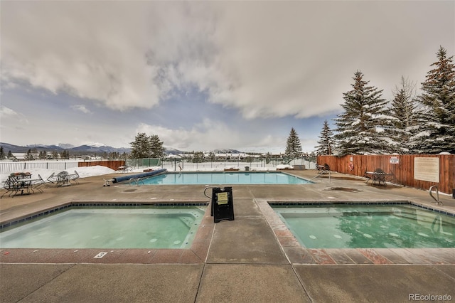 community pool featuring a patio area, a mountain view, an in ground hot tub, and fence