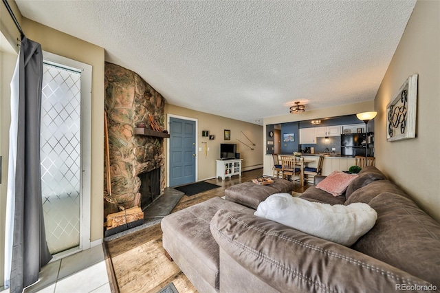 living area with a stone fireplace, a baseboard heating unit, and a textured ceiling