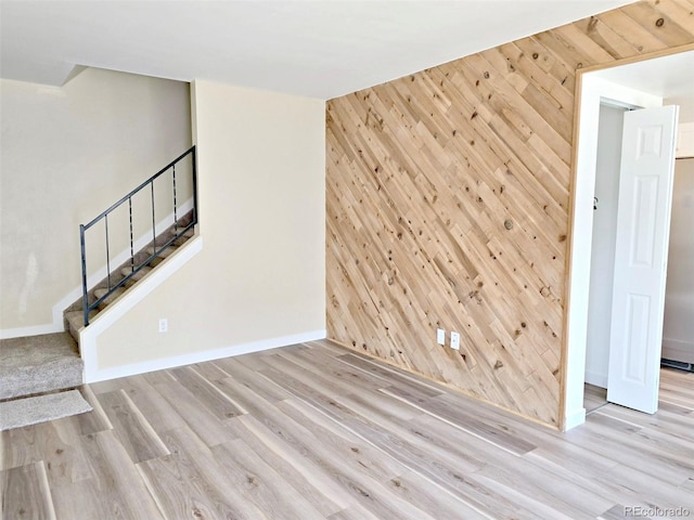 unfurnished living room featuring wood finished floors, stairs, wooden walls, baseboards, and an accent wall