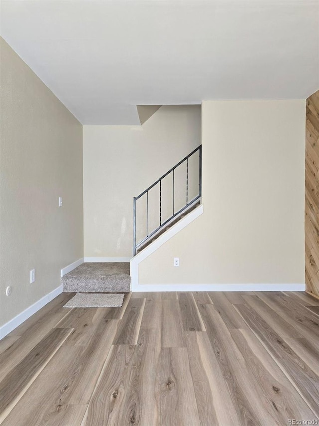 unfurnished living room with stairs, wood finished floors, and baseboards